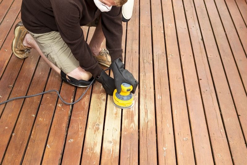 Local Newcastle carpenter sanding a deck surface with a power sander tool
