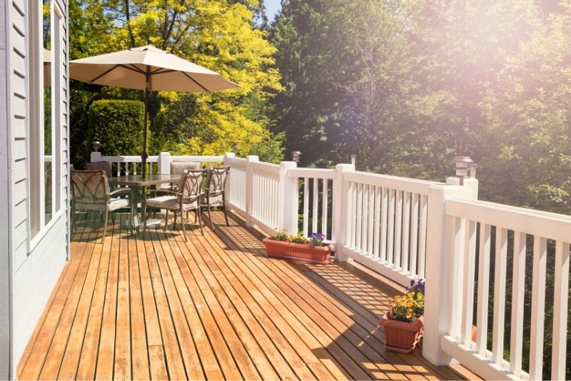 Above ground harwood timber deck with wooden white balustrade. There is a table with a beach umbrella and a few outdoor chairs at the back